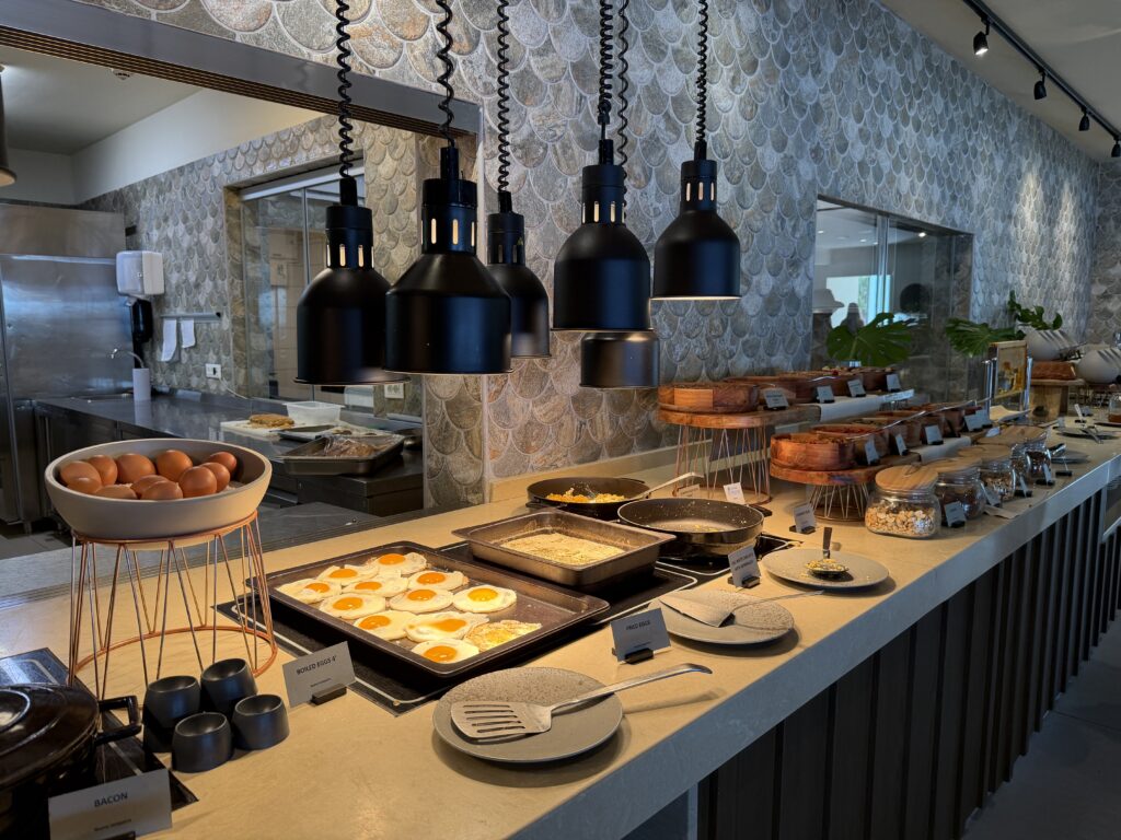 Buffet du petit-déjeuner avec œufs au plat, casseroles chaudes et décoration moderne sous lampes noires.