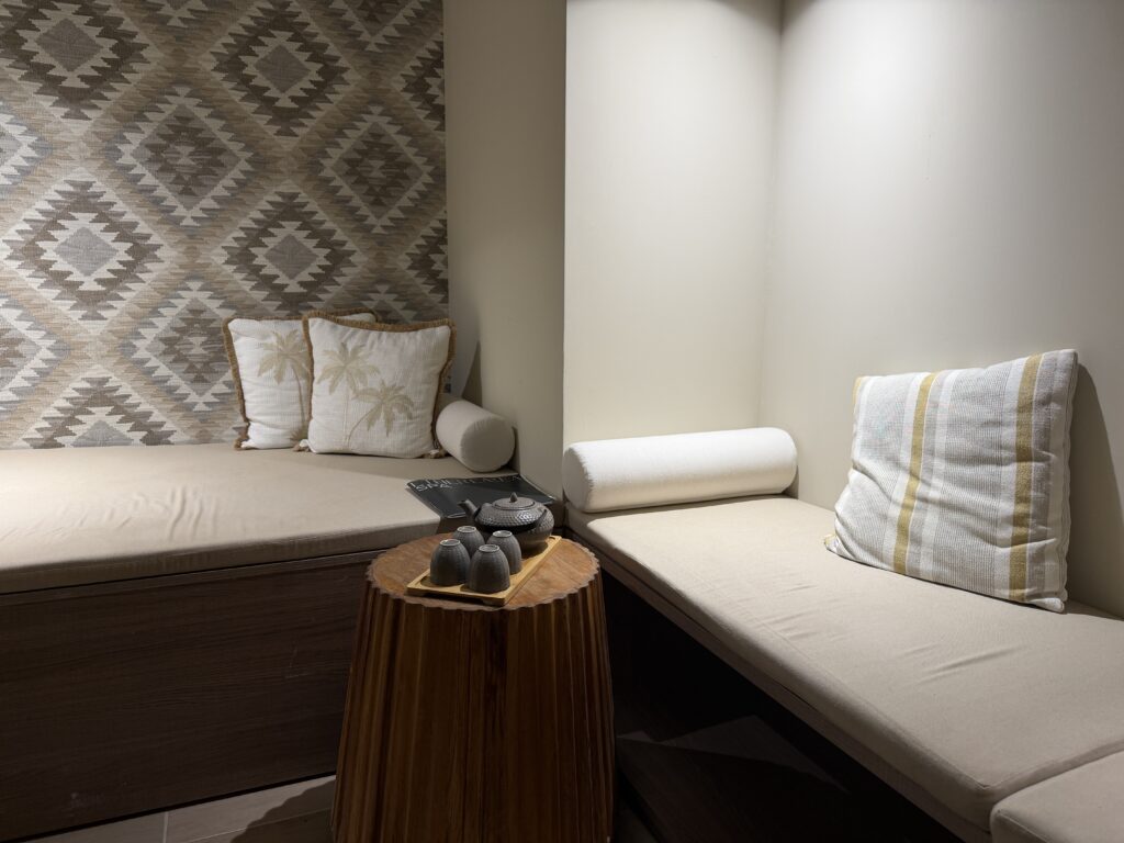 Coin salon cosy avec deux banquettes beiges, mur à motifs géométriques et table en bois.