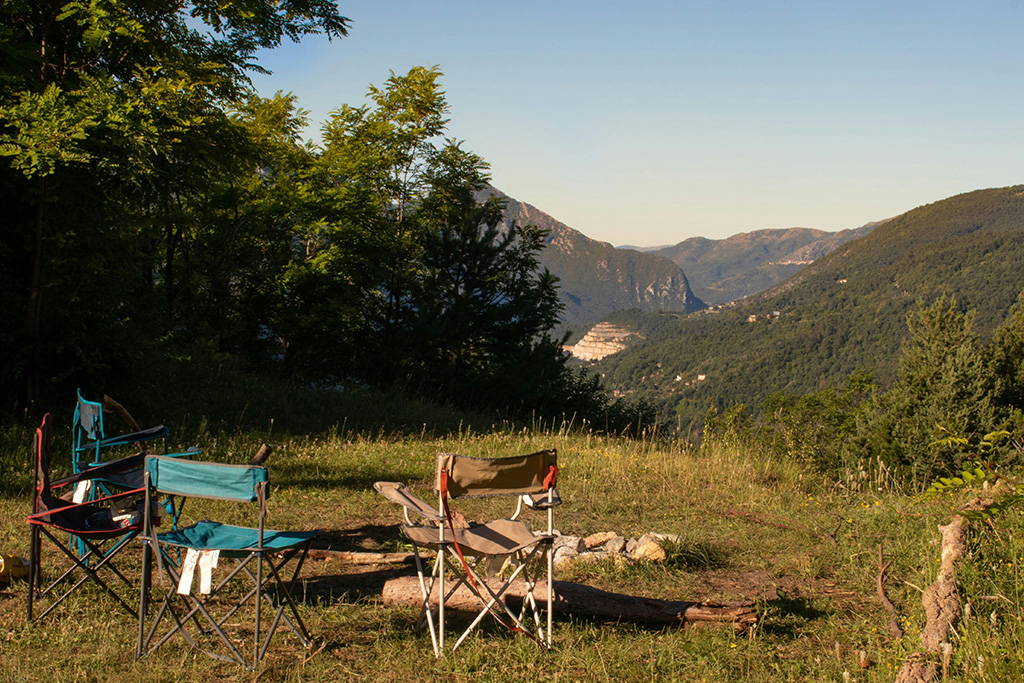 Quatre chaises de camping vides entourent un feu éteint avec vue sur des montagnes verdoyantes.