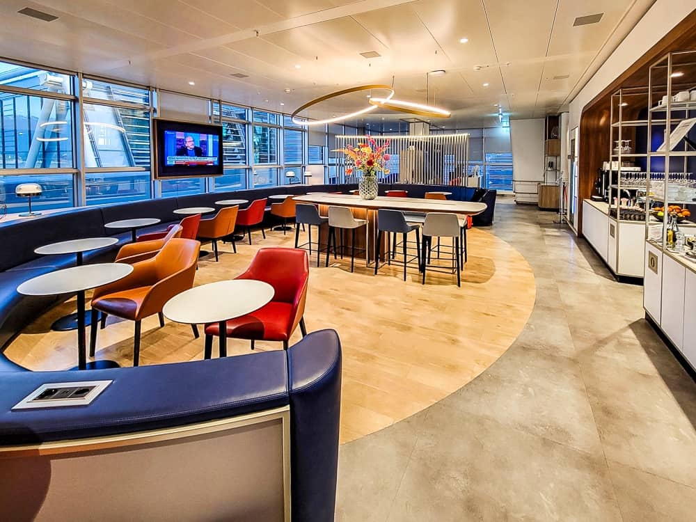 Vue large du salon avec banquette incurvée, cercle de parquet clair et table haute