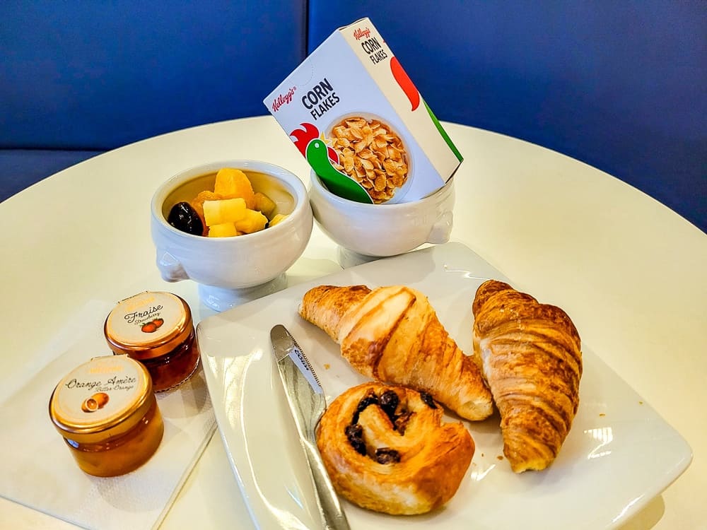 Assiette de viennoiseries, bols de fruits frais et Corn Flakes sur une table du salon