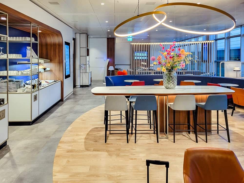Vue d'ensemble du salon avec table haute, buffet et suspension lumineuse circulaire