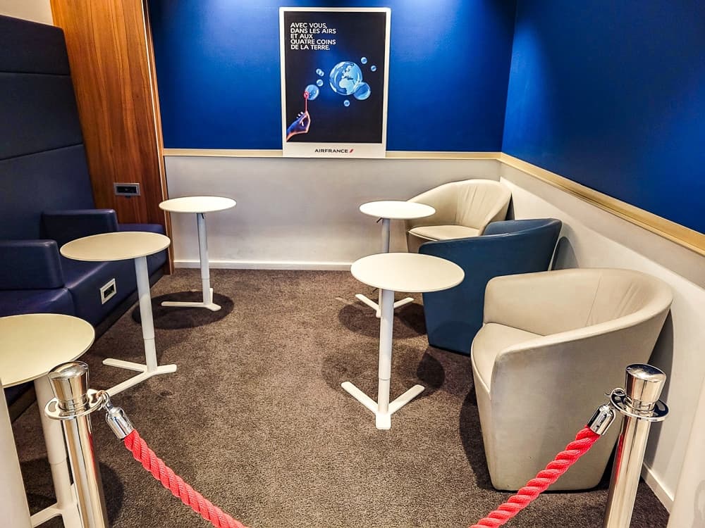Petit espace fermé par un cordon rouge, fauteuils beiges et affiche Air France au mur